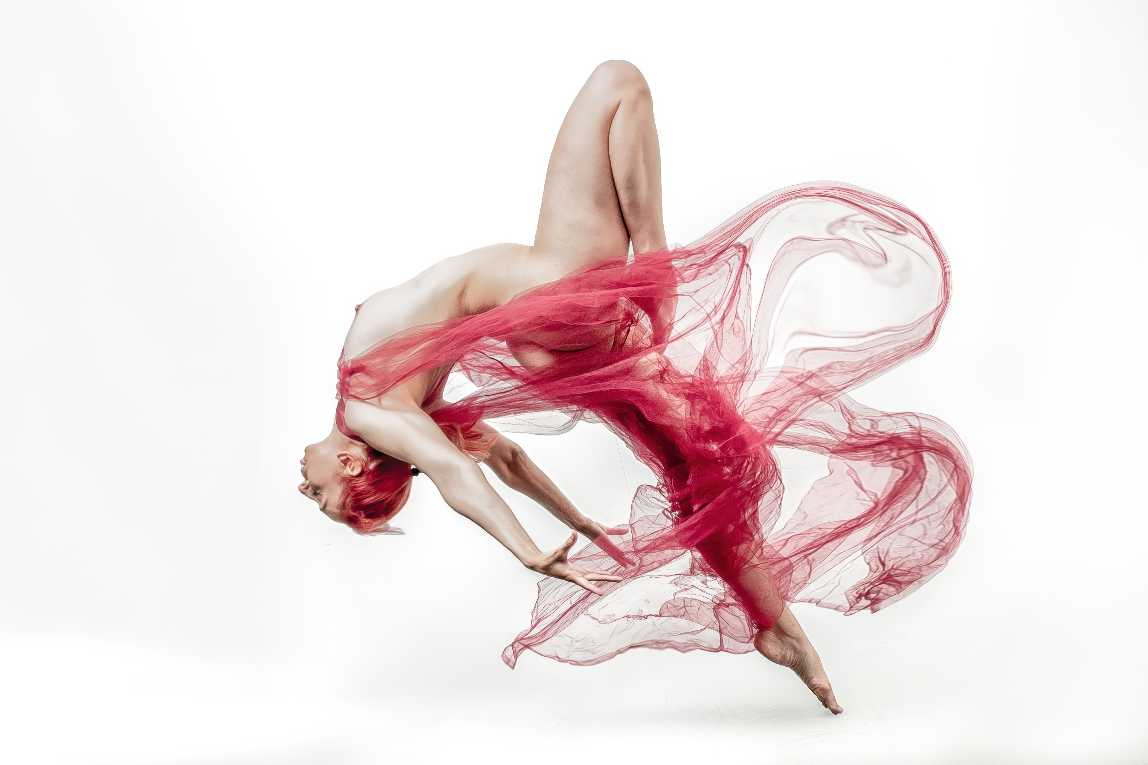 Künstlerisches Aktfoto einer Frau mit rotem Stoff in dynamischer Pose, die Eleganz und Bewegung ausdrückt.